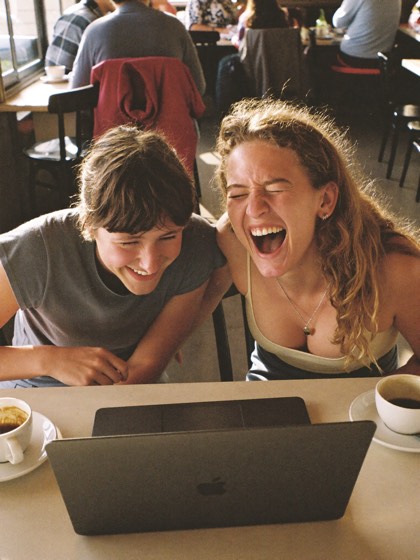 Dos creadores riendose de un blooper en la laptop de una cafeteria