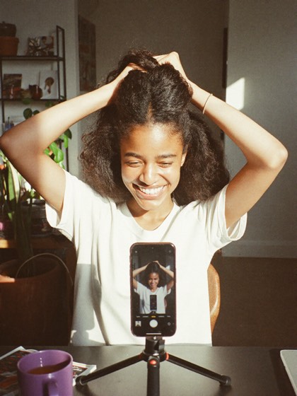 Creadora ajustandose el pelo sonriendo frente a su telefono en tripode, lista para grabar